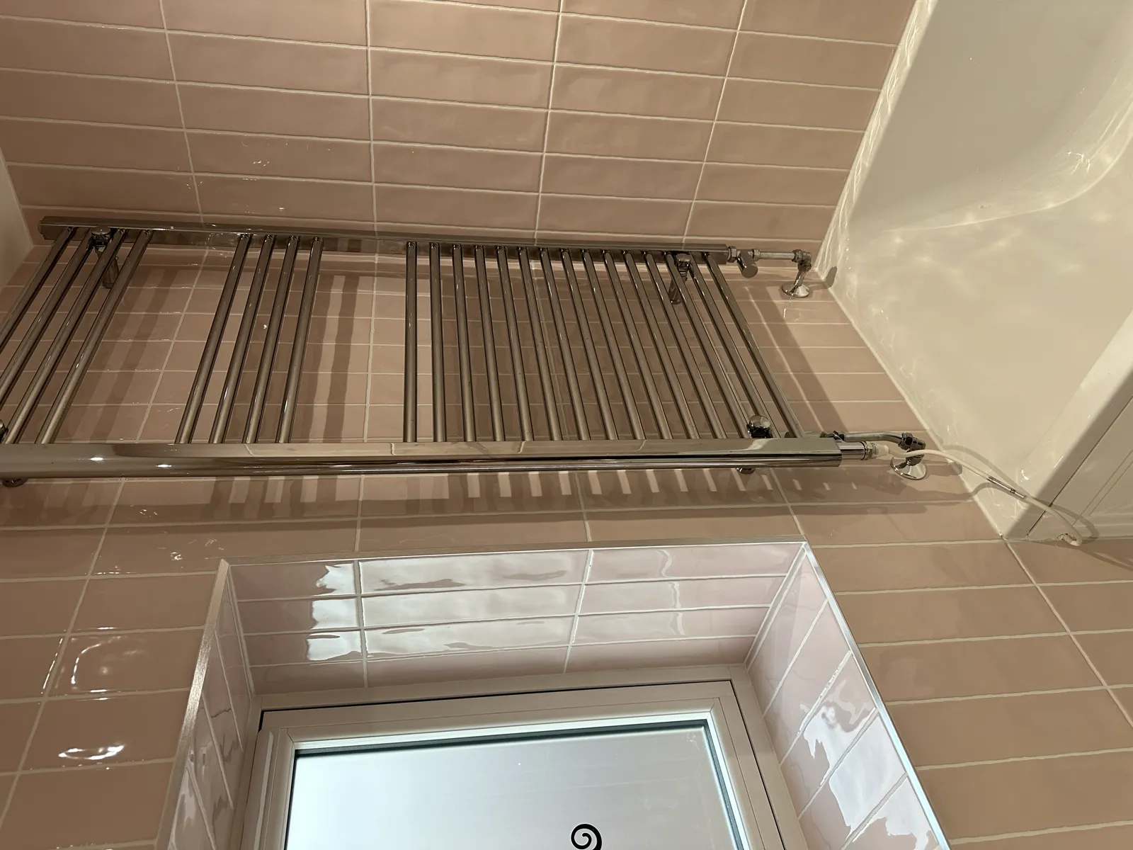 Blush pink gloss tiled bathroom with chrome heated towel rail