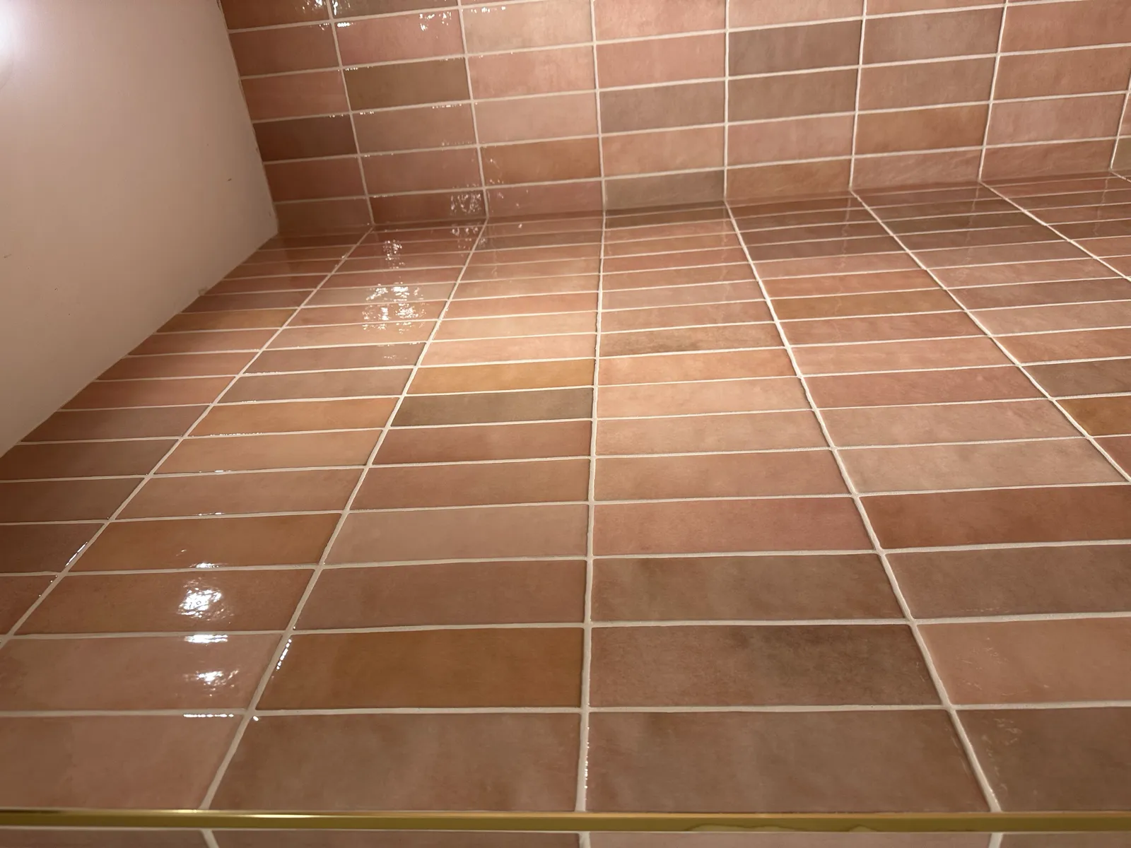 Warm terracotta gloss tiled bathroom walls and floor with brass edging